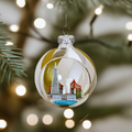 A clear glass globe ornament with a cityscape inside, featuring iconic landmarks such as the Transamerica Pyramid, Ferry Building, Coit Tower, Lombard Street, and Golden Gate Bridge, accented with gold and white glittery stripes, hanging on a Christmas tree.